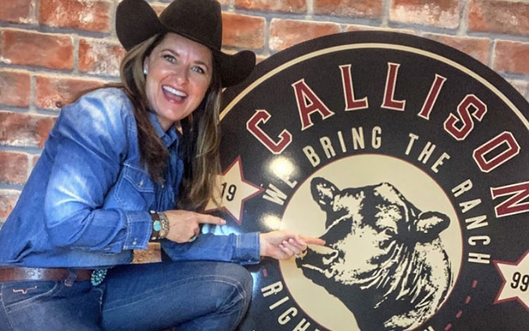 A cowgirl wearing a black cowboy hat posing with a circular sign that reads “Callison Ranch Beef”.